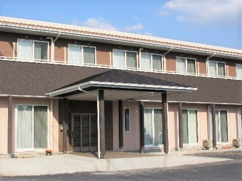 2階部分にベランダが付いた2階建ての建物はブラウン系。建物の玄関には段差がなく、車寄せが付いている。