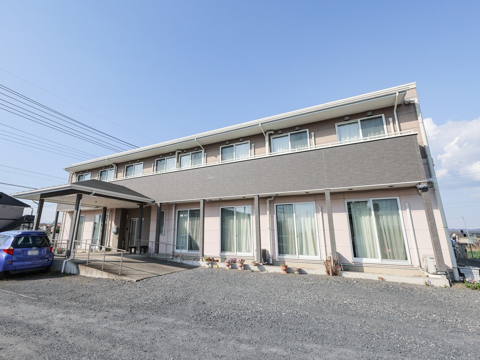 ブラウン系の2階建ての建物にはベランダが付き、玄関には車寄せがあり、段差も解消されている。日当たり良好で明るい雰囲気。