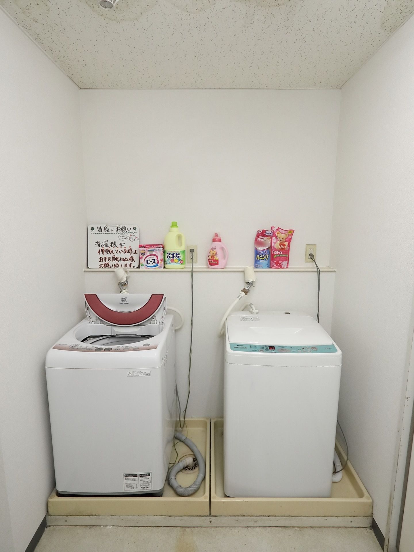 洗濯機が２つ用意され、台の上には漂白剤や洗剤、柔軟剤が用意されている。隅には、注意書きが置いてある。