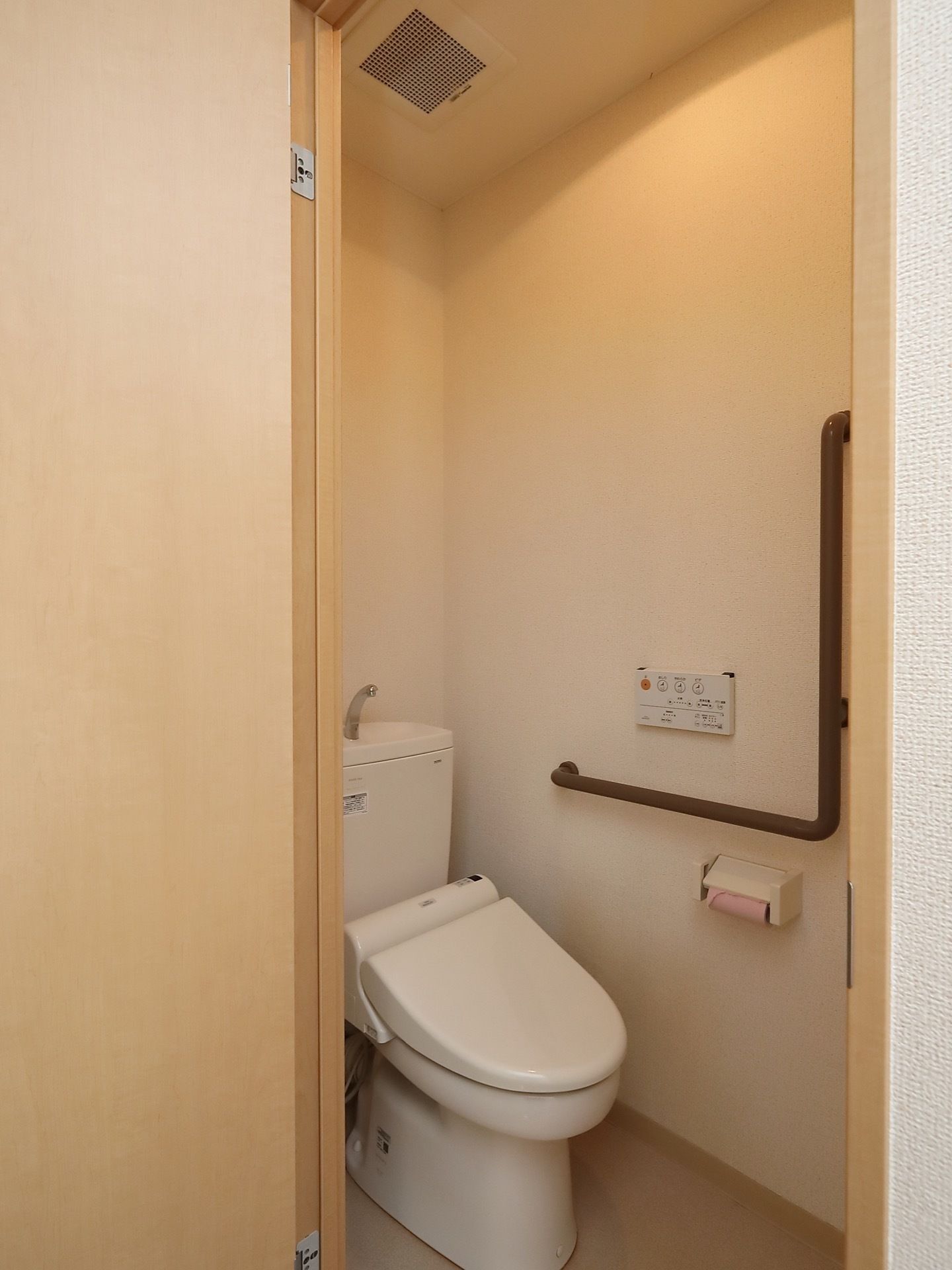 壁には手すりとともに、シャワー機能の操作盤がついていて、トイレットペーパーはピンク色である。タンクには手洗い機能がついている。