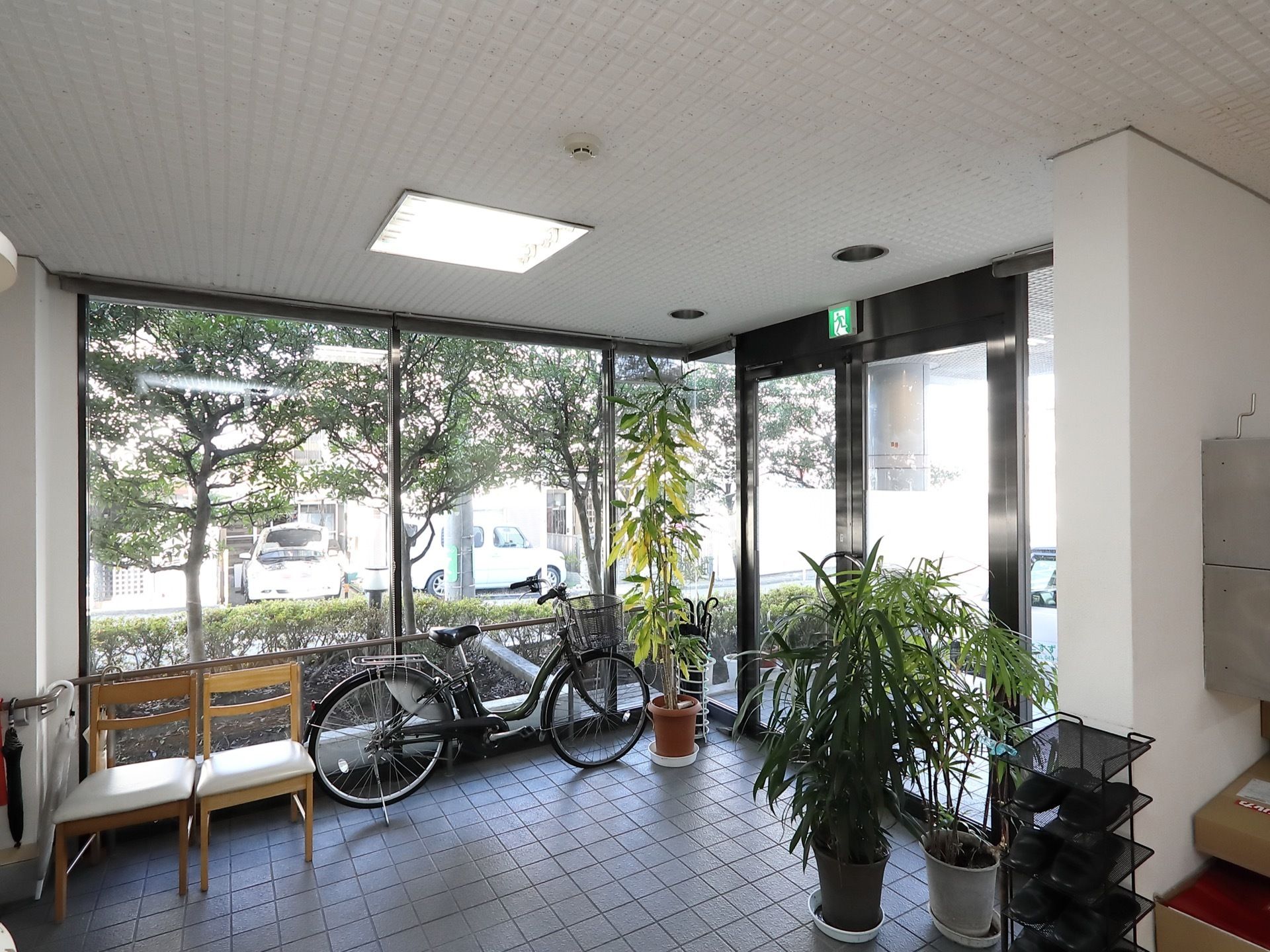 大きなガラス張りの玄関で、外の様子がよく見える。土間には椅子２脚と自転車、観葉植物、スリッパラックが置いてある。