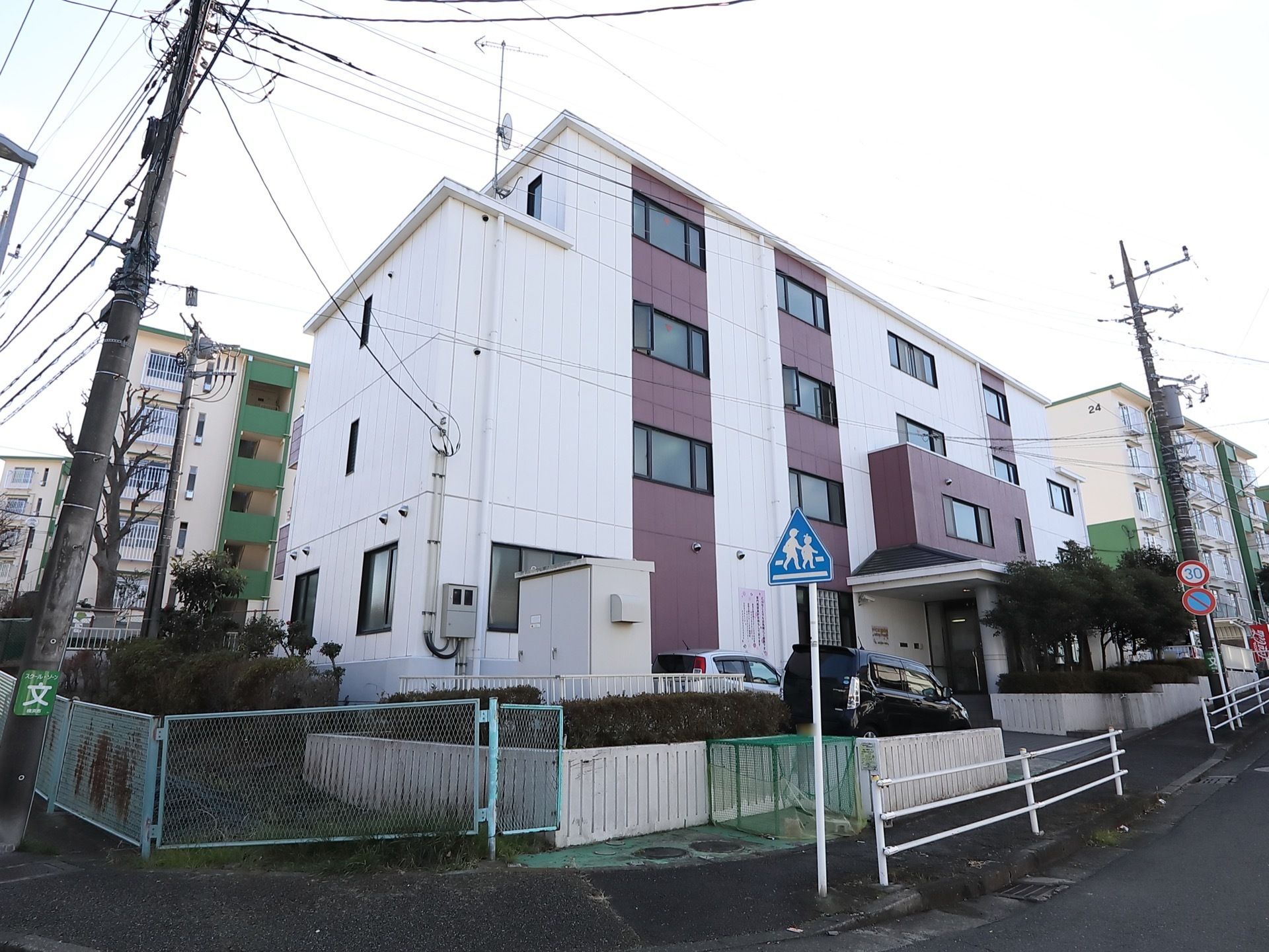 ４階建てで、白と茶色のスプライト模様である。玄関のすぐ前には駐車スペースが２台分用意されており、車が停まっている。