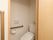 トイレは温水洗浄便座となっている。壁に茶色い横型の手すりと操作パネル、ペーパーホルダーが設置されている。