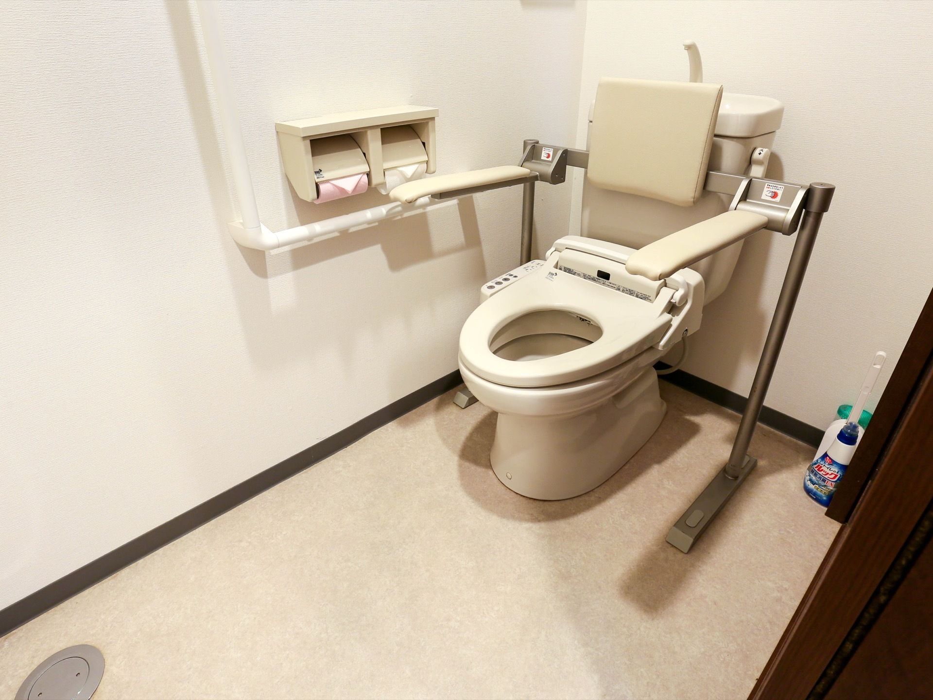 十分なスペースを確保したトイレである。L型手すりや温水洗浄便座、背もたれ付きアームレストが完備されている。
