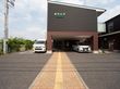 ２階建ての大きな建物がある。一階部分が駐車スペースになっており、外にも車が停まっている。玄関に向かって点字ブロックが敷かれている。