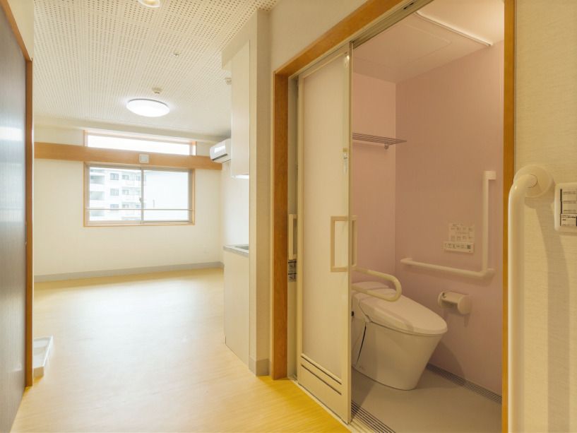 フローリングの部屋には家具や家電はなく、手前にはエル字型の手すりが付いた広いトイレがあり、大きなスライド式のドアが付いている。