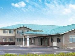 広い駐車場がある敷地にブラウン系の建物が建っている。車寄せも付いている。