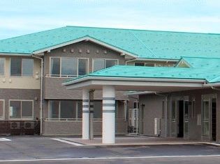 緑の屋根が付いたブラウン系の２階建ての建物には大きな車寄せと駐車場が付いている。