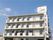 4階建ての建物は白を基調としていて清潔感がある。住宅名が書かれた縦の看板が建物の横にあり、建物の上にも住宅名が書かれている。