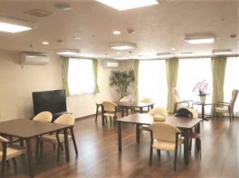 広めの空間に四人掛けのテーブルと椅子が複数組並んでいる様子。テレビとエアコンがある空間