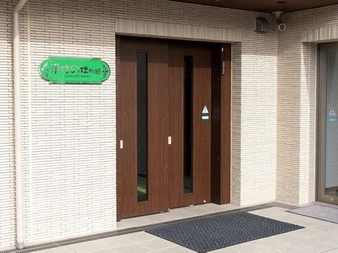 緑色のプレートには住宅名が書かれ、玄関の横の外壁に貼られている。ブラウン系のドアは自動ドア。