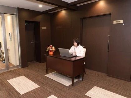 女性スタッフがエントランスのそばにあるデスクにつきパソコンで何かをしている様子。