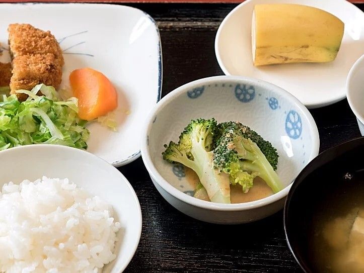 黒いトレーに並べられた食事。白いご飯に汁物、メインの揚げ物にブロッコリーのあえ物など。