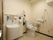 温水洗浄便座器とオストメイトが完備されたトイレである。壁にはL字型手すりや可動式手すりが設置されている。