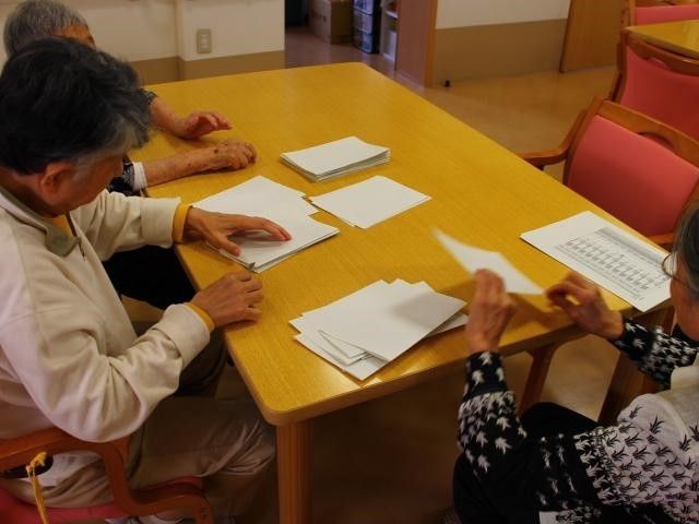 白い紙をテーブルの上で追っている３人の入居者の様子。