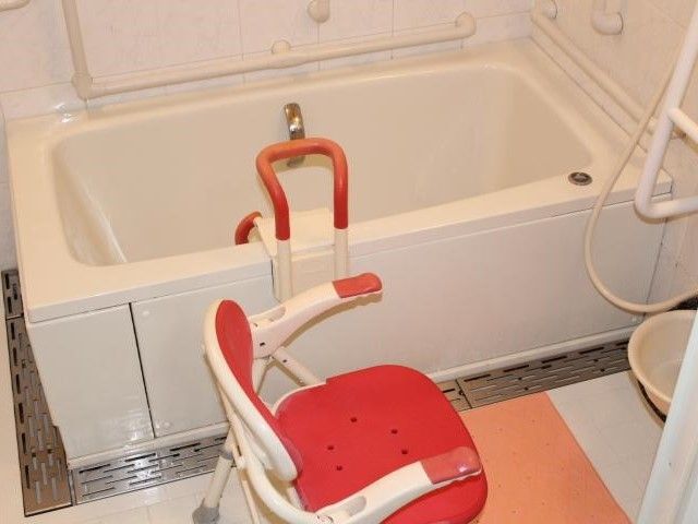 白い浴槽の横には手すりが設置され、シャワーの前にはシャワーチェアが置かれ、浴槽には可動式の手すりもある。