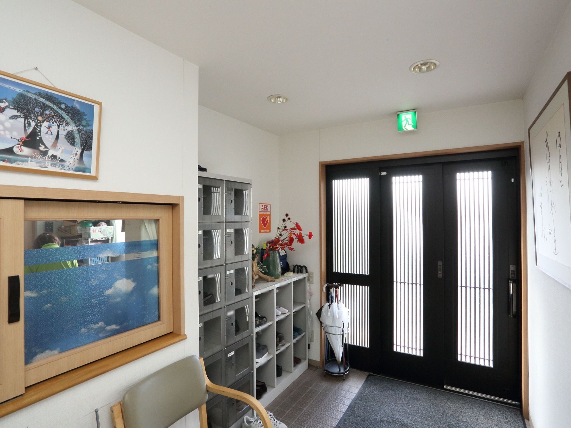 入口扉は格子状の引き戸になっている。玄関マットが敷かれ、傘立てが置かれている。壁に下駄箱があり、扉付きのものとロッカータイプのものがある。