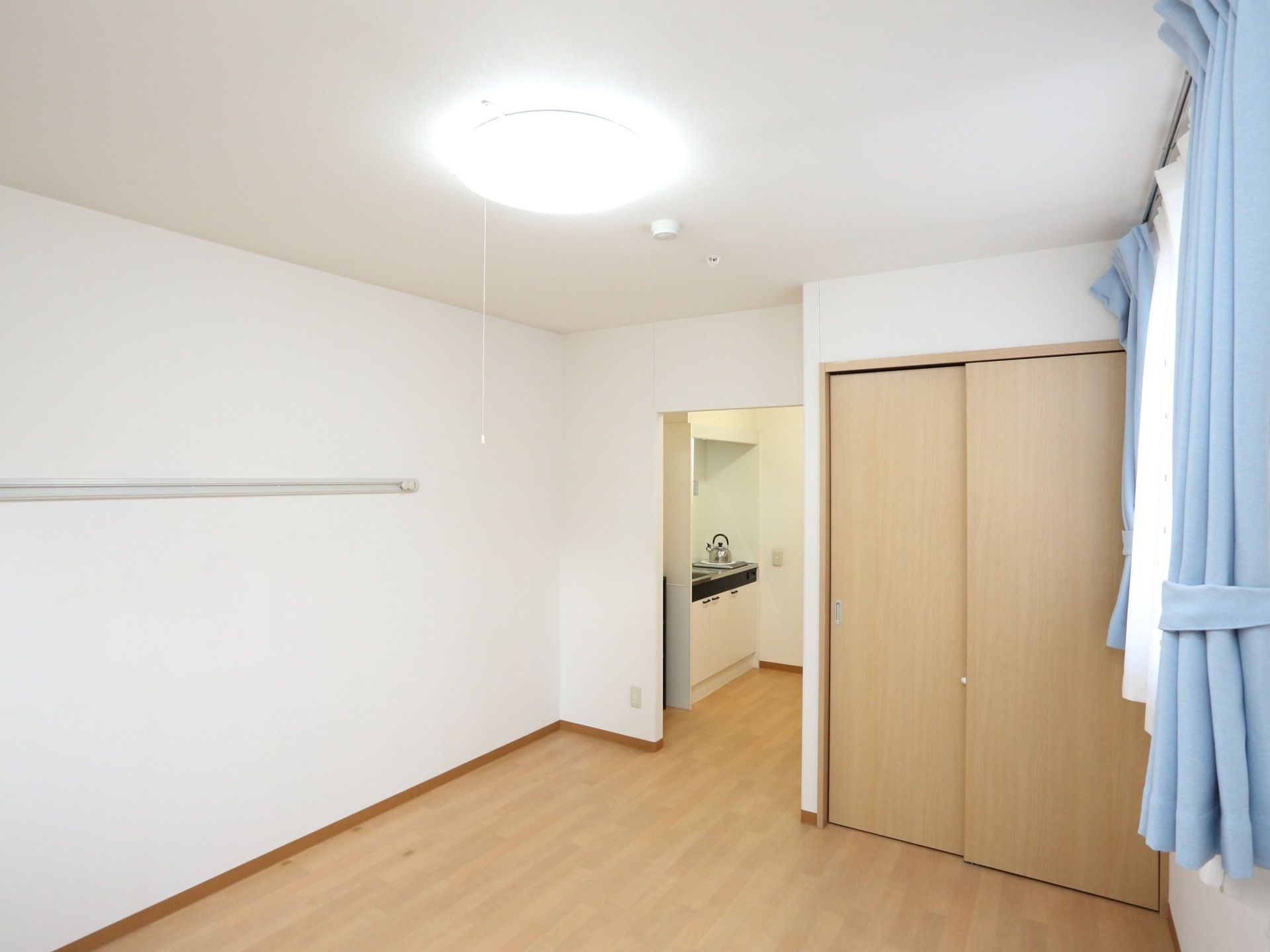 居室へ入ると入口横にキッチンがある。居住スペースには押し入れタイプの収納がある。壁にレール式のフックが取りつけられている。