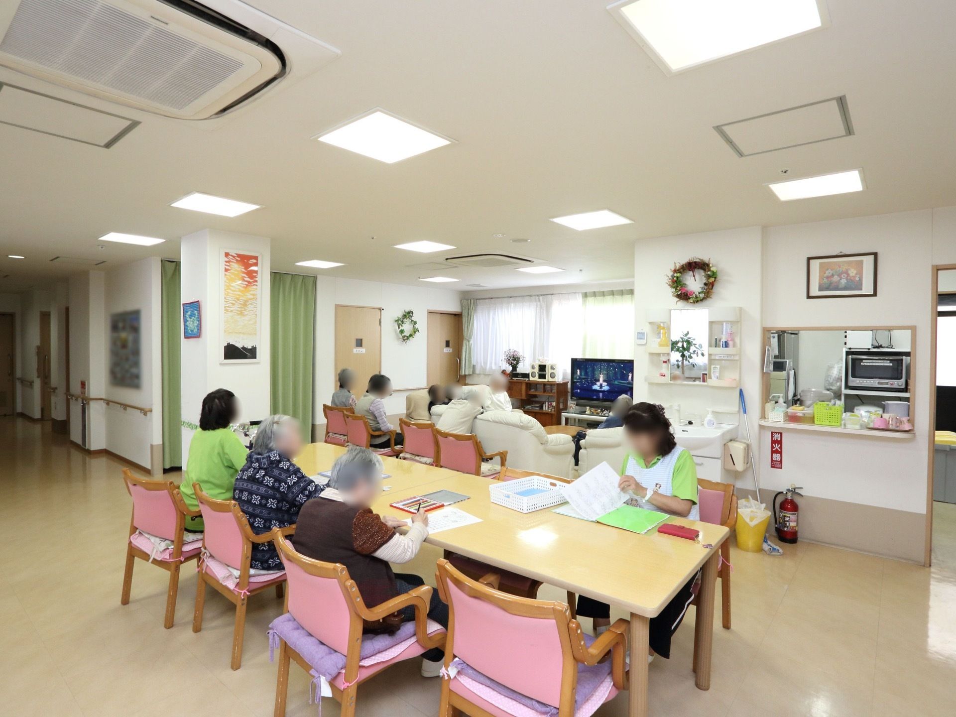 共有スペースに、テーブルやソファ、椅子が多く置かれている。作業しているスタッフのそばで、入居者様が創作活動を行っている。
