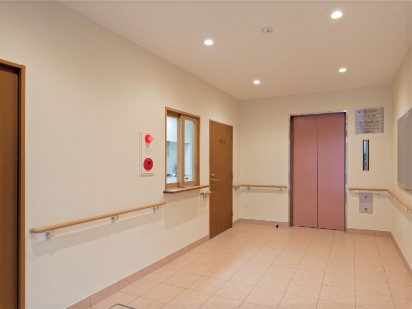 ピンクのエレベーターが設置された館内。壁には木製の手すりが付き、左側にはスタッフが常駐するステーションがある。