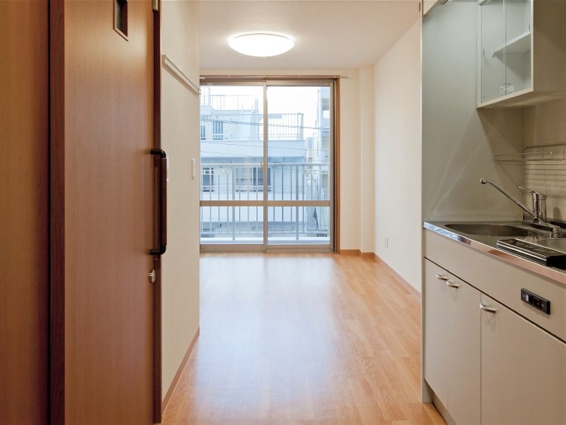 フローリングのワンルームタイプの部屋。右側にはオール電化のキッチンがあり、左側にはトイレのスライド式のドアがあり、ベランダも付いている。