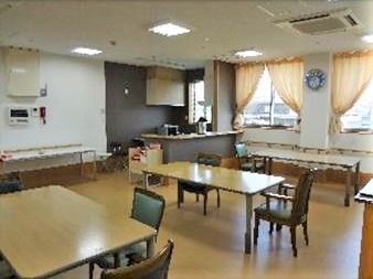 ダイニングテーブルが複数並んだ食堂は窓が多く明るい。奥にはキッチンもある。