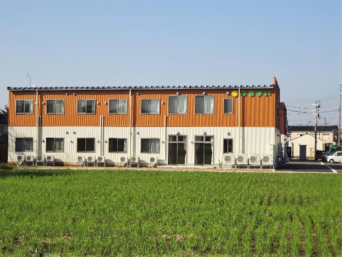 駐車場付きの広い敷地にたたずむ2階建ての建物。外壁には住宅名が書かれている。