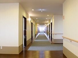 手すりが設置されたまっすぐな廊下の両サイドに居室のドアがあり、突き当りには窓がある。