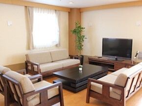 テレビが設置され、ローテーブルを囲むようにベージュのソファが置かれているフローリングの共有スペース。