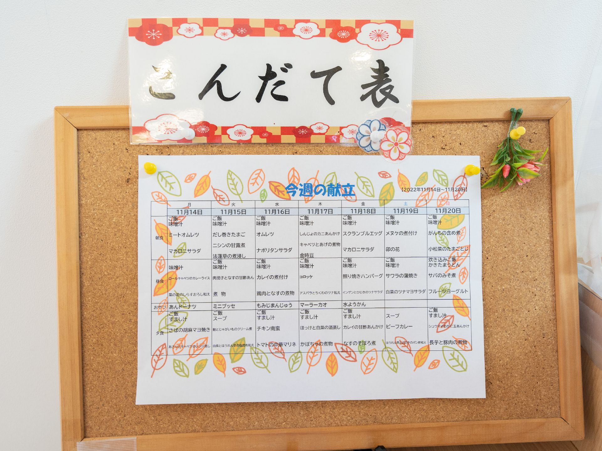 カーディガンを着た高齢女性とピンクのエプロンを付けた若い女性スタッフが笑顔で過ごしている。