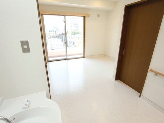 大きな木製のドアが付いたシンプルな部屋。窓にカーテンはなく、洗面所がある。