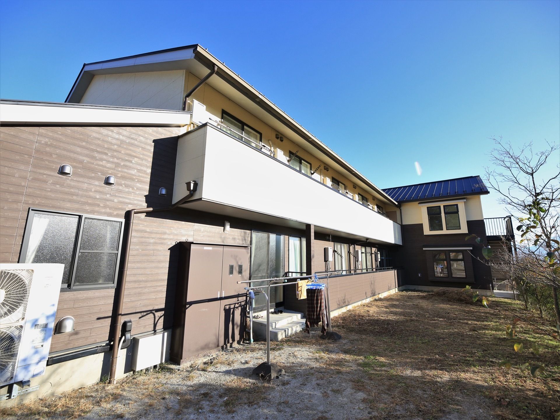 ２階建ての建物は、濃い色と明るい色合いで入居者様に温もりを与えてくれる。ベランダが設置されているので、洗濯物を干すことができる。