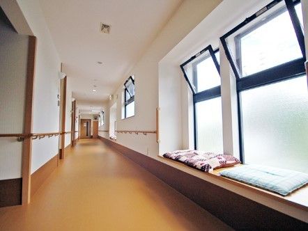 幅の広い手すり付きの廊下の様子。窓際に休憩用の座布団が置いてあるベンチスペースがある