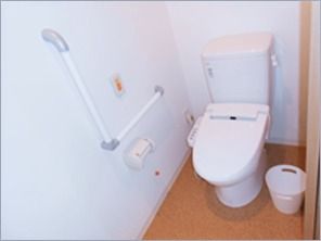 白い温水便座が設置されたトイレにはごみ箱や手すり、呼び出しボタンがある。