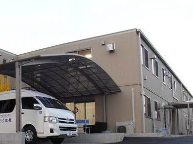 カーポートがあり白い車が止まっている。その奥にはブラウンの外壁の2階建ての建物がある。