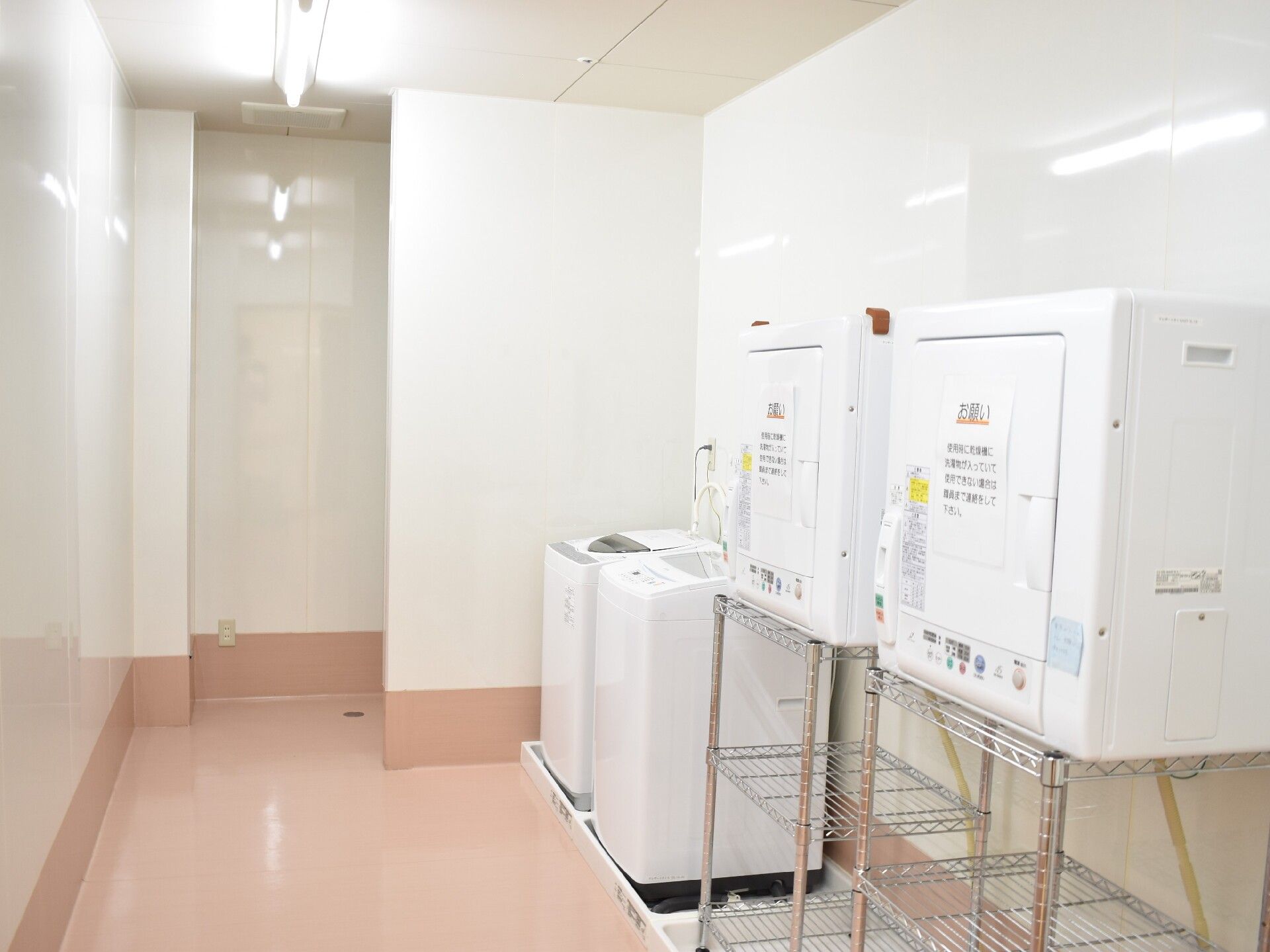壁は白で床はピンクの部屋に洗濯機2台と乾燥機が2台置かれている。