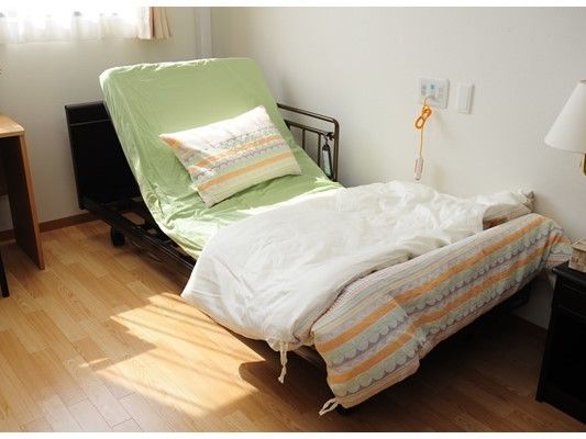 ベッドは電動式の介護ベッド。大きな窓があり日当たりのいい部屋には収納家具なども置かれている。