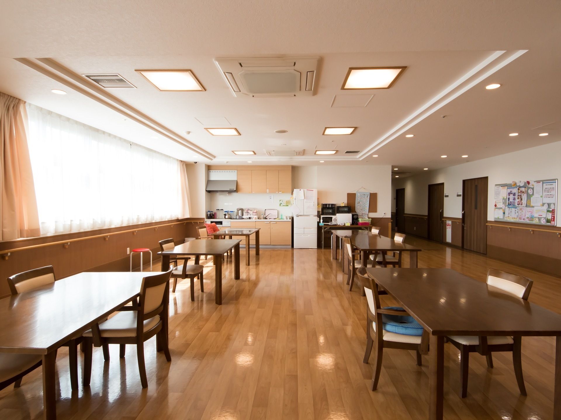 開放感たっぷりの窓が設置された、明るい食堂である。突き当りにはシステムキッチン、冷蔵庫などが置かれている。