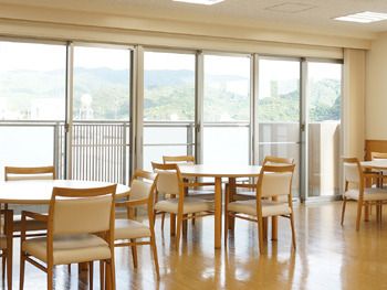 大きな窓が付いた明るい雰囲気のリビングダイニング。窓の外には緑が広がり、室内にはダイニングテーブルが複数ある。