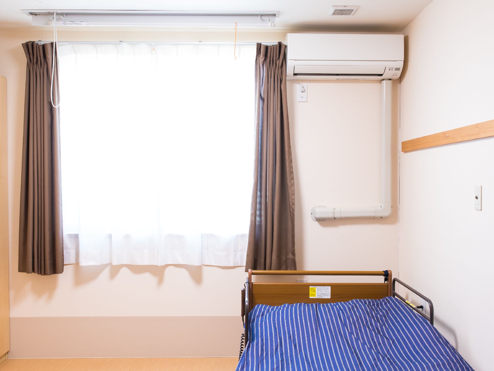 腰高窓に茶色のカーテンが付けられた、エアコンやベッドが設置されている居室