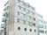 レンガが全面に貼られた６階建ての建物で、２階部分には丸い窓が４つ並んでいる。施設前には通りがあり、低木が植えられている。