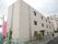 ３階建ての建物を右斜め前から撮影。建物の左側にはピンクの看板が設置されている。