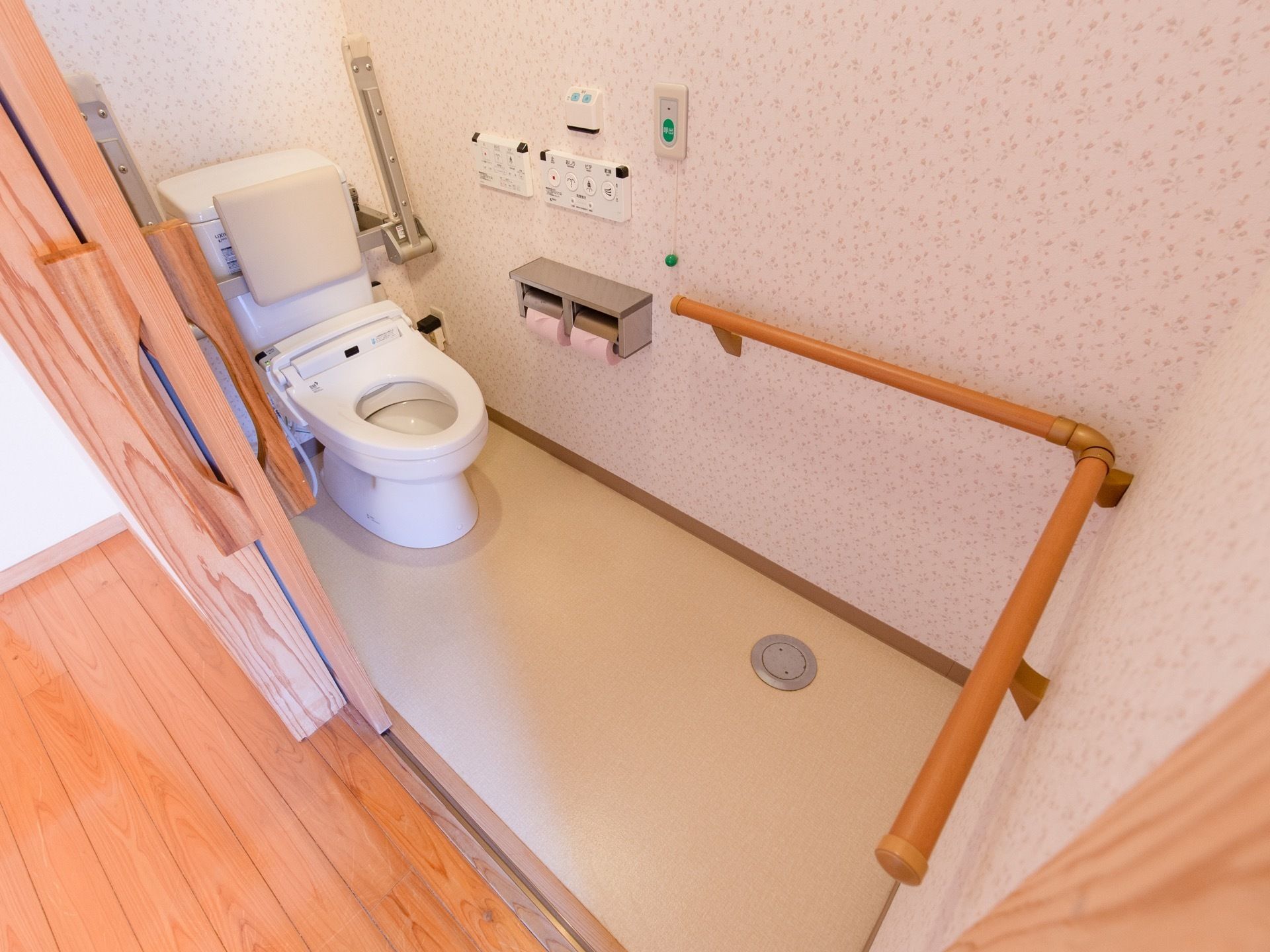 引き戸を開けた所にトイレが設置されている。背もたれや可動式のひじ掛けがある。入口から便座の近くまで切れ目なく手すりがある。
