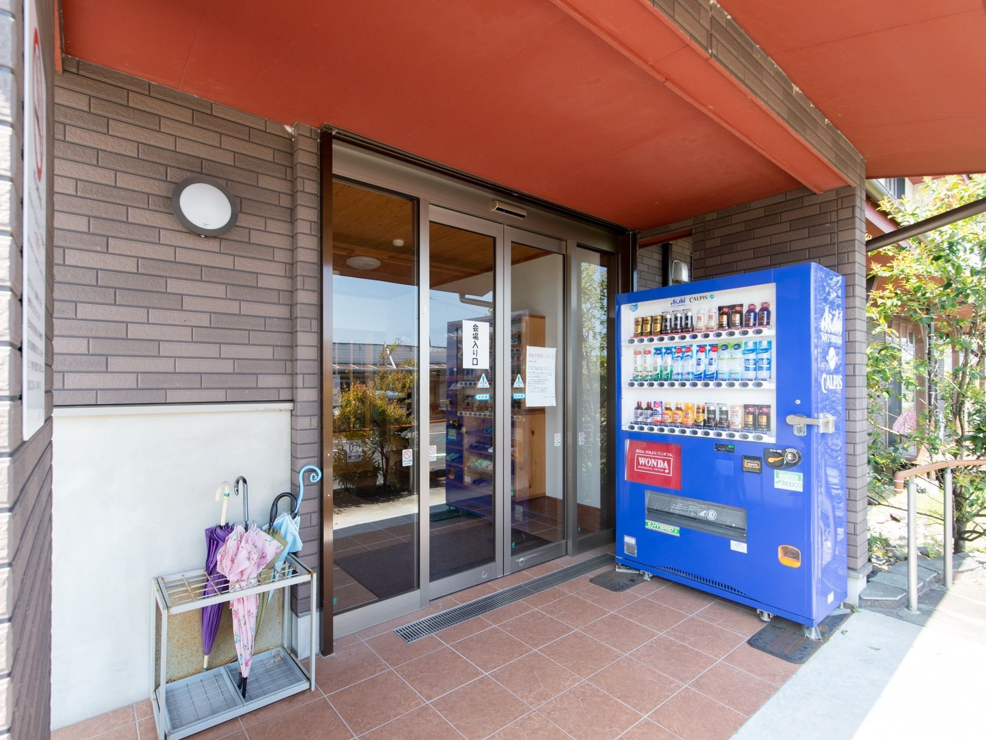 玄関はガラスの両開きの自動扉になっている。入口の右側には飲料の自動販売機が、左側には傘立てが置かれている。