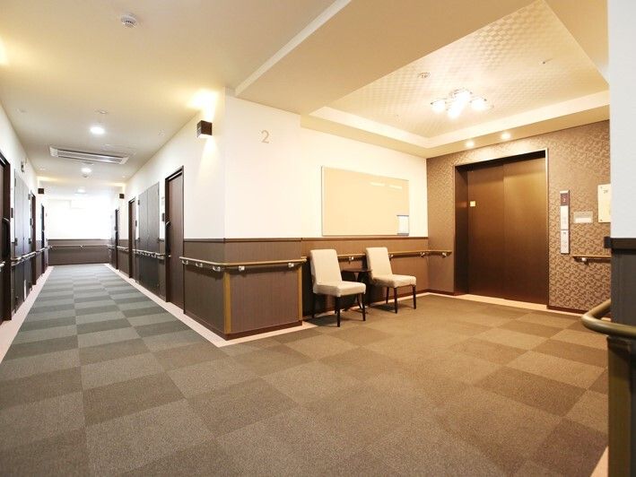 エレベーターが設置された館内。エレベーターホールには白い椅子があり、壁には手すりが付いている。