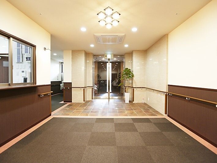 広々としたエントランスには自動ドアが設置され、左側には管理室があり、壁には手すりが付いている。