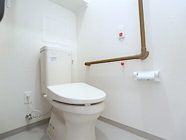 白でまとめられたトイレにはダークブラウンの手すりが付き、オレンジの呼び出しボタンも設置されている。
