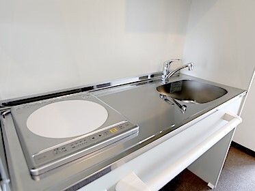 ステンレス製の流しが付いたキッチンにはIHクッキングヒーターが付き、足もとにスペースがある。