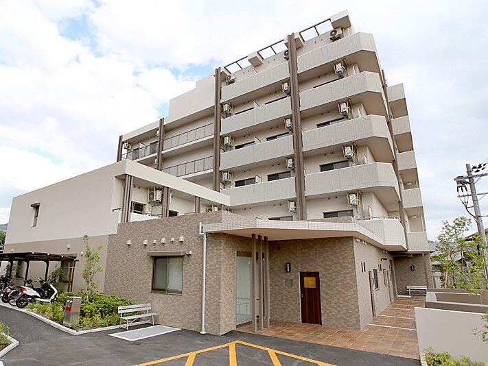 ベージュ系のどっしりとし建物の各フロアにベランダがあり、玄関先には屋根が付いている。