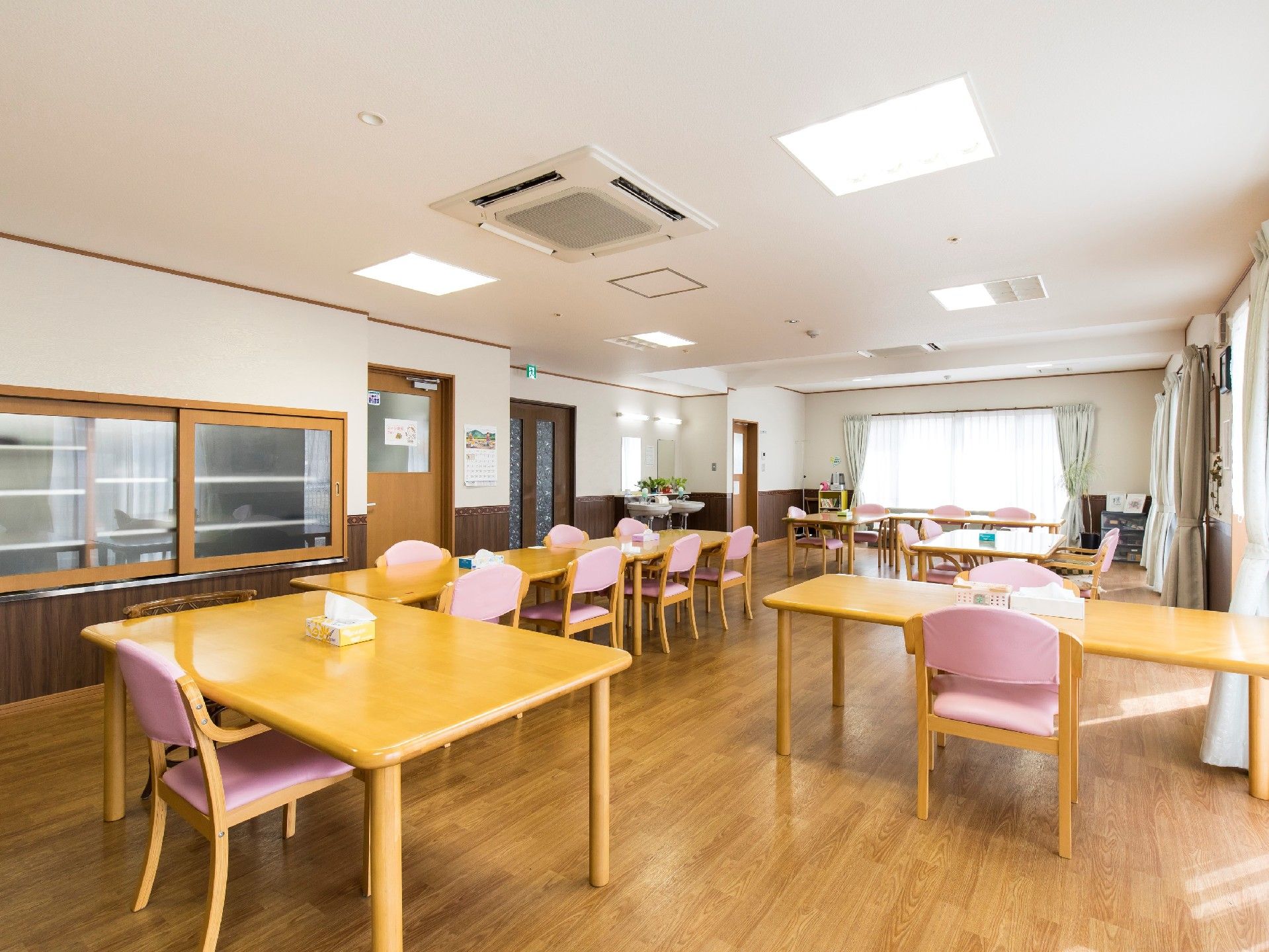 木製のテーブルに、ピンクの座面の椅子が置かれた部屋。奥には大きな窓がある